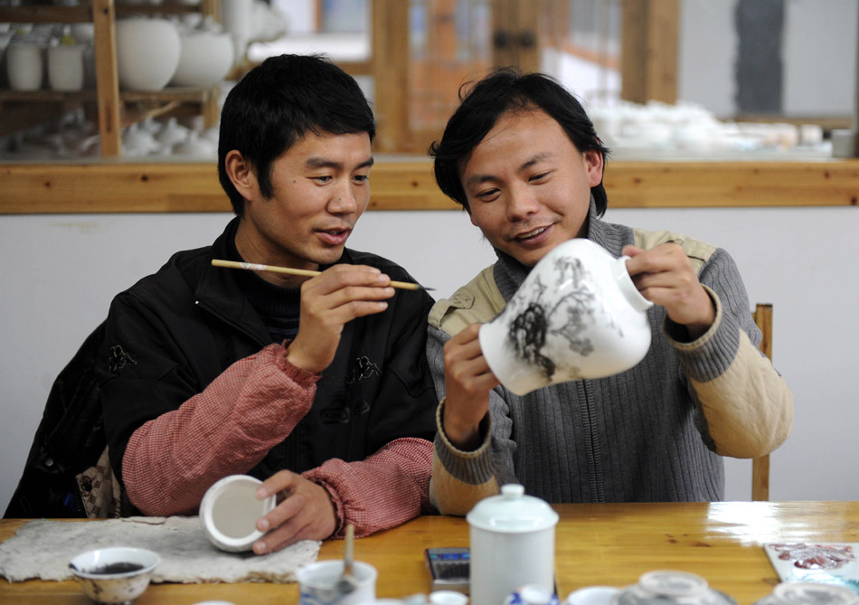 Liu Zhen (R) discuses painting techniques with another painter in Jingdezhen of east China's Jiangxi Province, March 8, 2012. (Xinhua/Zhou Ke)