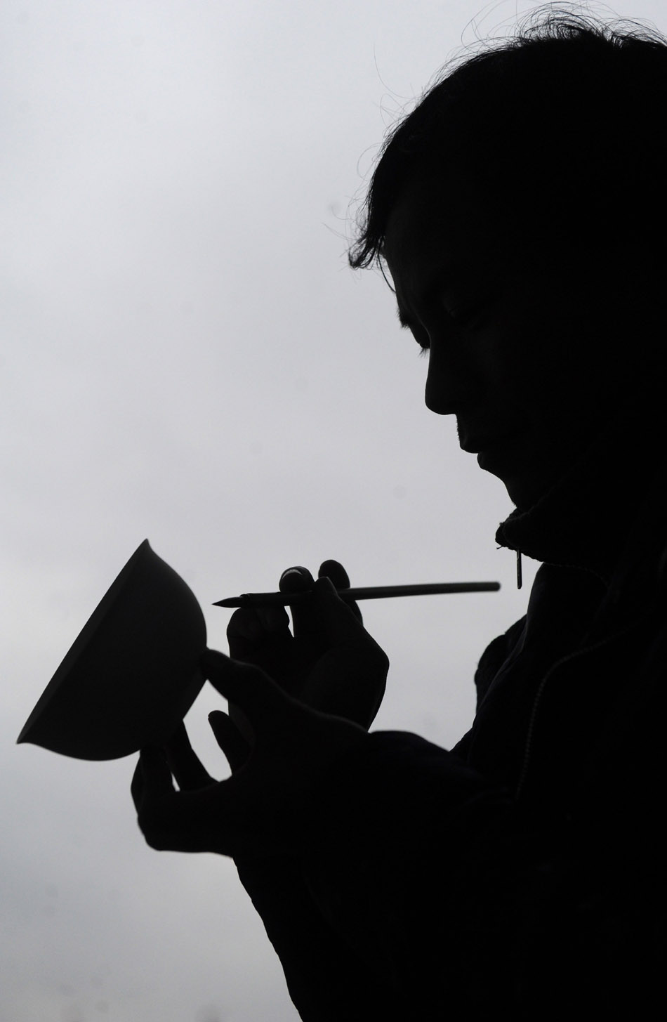 Liu Zhen is silhouetted as he painting on a  porcelain adobe in his studio at the Chengdexuan Porcelain Co.,Ltd, in Jingdezhen of east China's Jiangxi Province, March 8, 2012. (Xinhua/Zhou Ke)