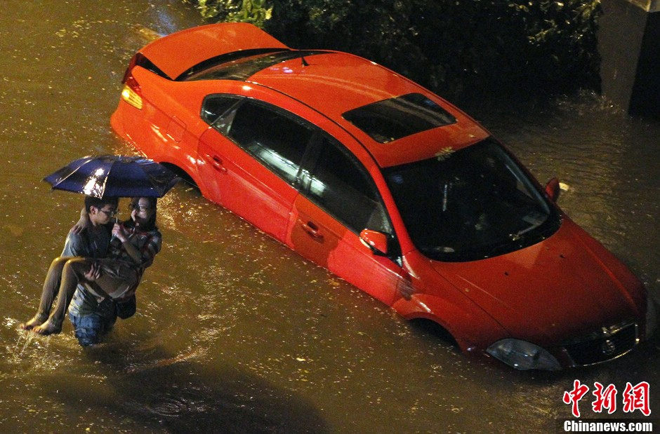 A man carrying his girlfriend wades in deep stagnant water on the road. (Chinanews/ Ren Chenming)