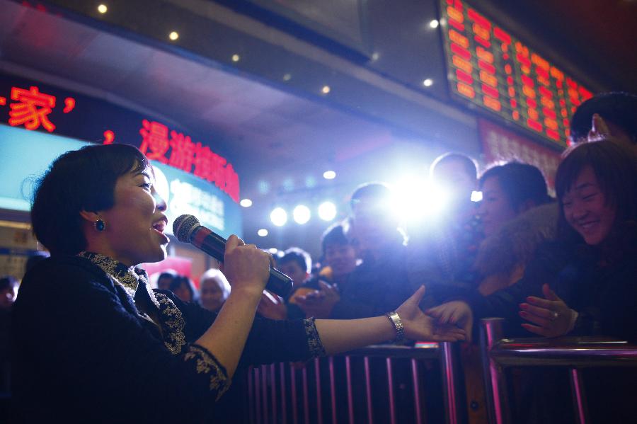 A volunteer (1st L) interacts with the passengers as she performs for the crowd at the station in Hangzhou, capital of east China's Zhejiang Province, Jan. 23, 2013. A group of volunteers visited the train station in Hangzhou, offering the passengers hot ginger beverage, snacks and Spring Festival Couplets. Stations in Hangzhou embraced more passengers ahead of the Spring Festival travel peak. (Xinhua/Cui Xinyu) 