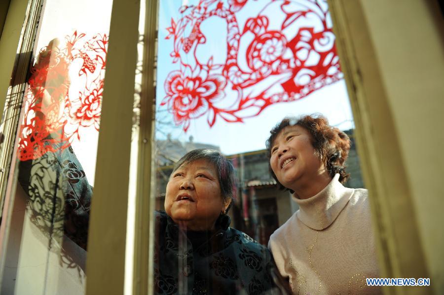 Liu Lanfang (L) attaches a piece of paper cutting work to the window of her home in Shenmu County of northwest China's Shaanxi Province, Jan. 28, 2013. People began to make paper cuttings for the decoration of the upcoming Spring Festival here in recent days. (Xinhua/Li Yibo) 