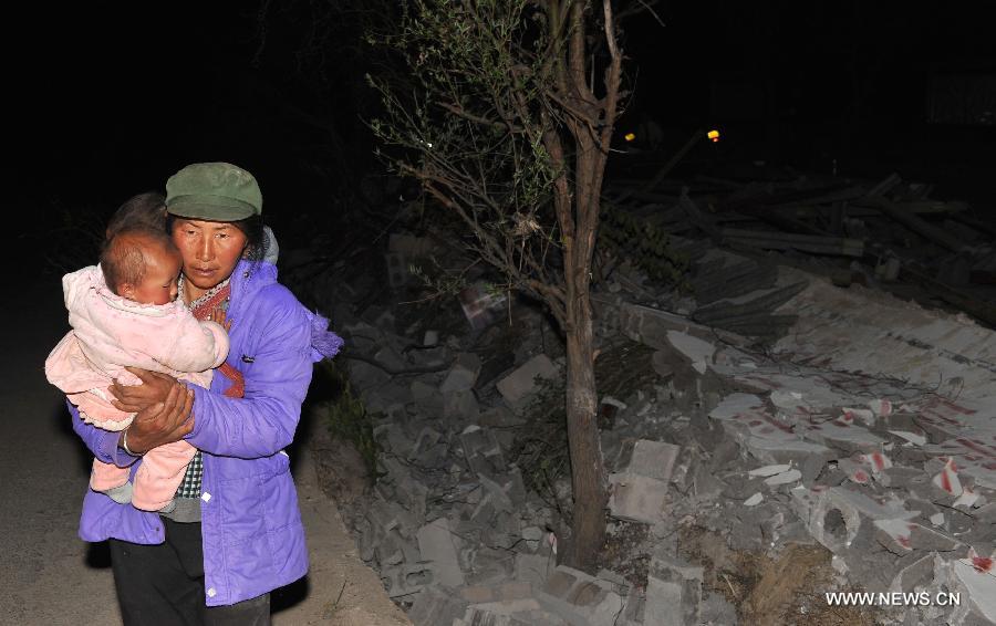 Local resident Yang Yuying carries her children as she walks past a piece of collapsed wall after a 5.5-magnitude earthquake in Eryuan County of Dali Bai Autonomous Prefecture, southwest China's Yunnan Province, on March 3, 2013. The number of people confirmed injured by a 5.5-magnitude earthquake that hit southwest China's Yunnan Province on Sunday afternoon has risen to 30, local authorities said. (Xinhua/Lin Yiguang) 