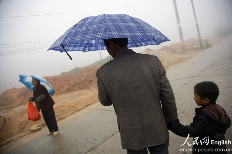 Bing's mother stops and chats with their neighbors on the way, while Bing moves on with his children silently on April 4, 2013. They seldom talked with other villagers since HIV infection. (CFP/Pan Deng)