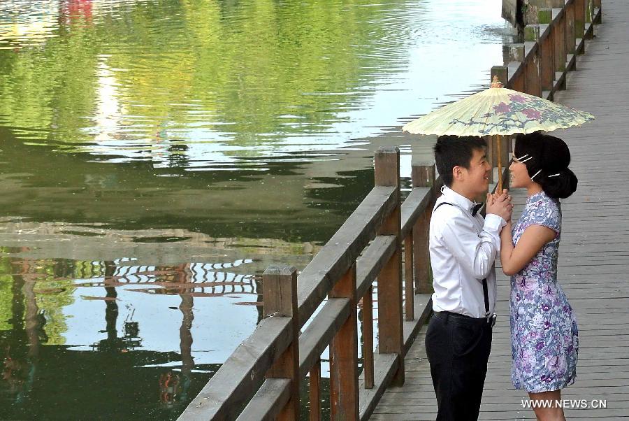 Two young stands under an umbrella for photos near a lake in Sanhe Town of Feixi County, east China's Anhui Province, April 24, 2013. The Sanhe Ancient Town, which has a history of more than 2,500 years, is a typical "ancient town full of rivers and lakes, together with small bridges, flowing water and local dwellings." (Xinhua/Wang Song)