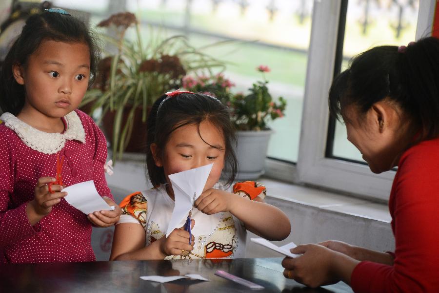 A volunteer leads left-behind children, whose parents go to other places to work, do the paper-folding assignment at an after-school care center in Yanji City, Yanbian Korean Autonomous Prefecture in northeast China's Jilin Province, May 22, 2013. More than 30,000 children are left behind by their parents who choose to go to South Korea to work in the Yanbian Korean Autonomous Prefecture. The local government established 20 after-school care centers to provide these left-behind children with the after-class care. (Xinhua/Lin Hong)