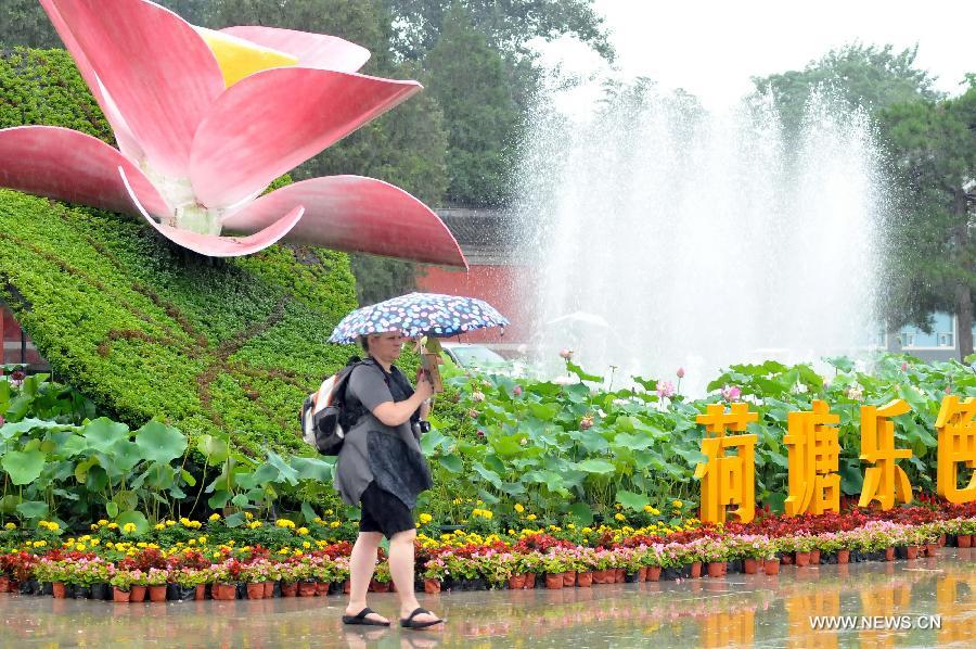 A foreign tourist walks past lotus flower decorations at Yuanmingyuan, the Old Summer Palace, in Beijing, capital of China, July 10, 2013. (Xinhua/Feng Jun)