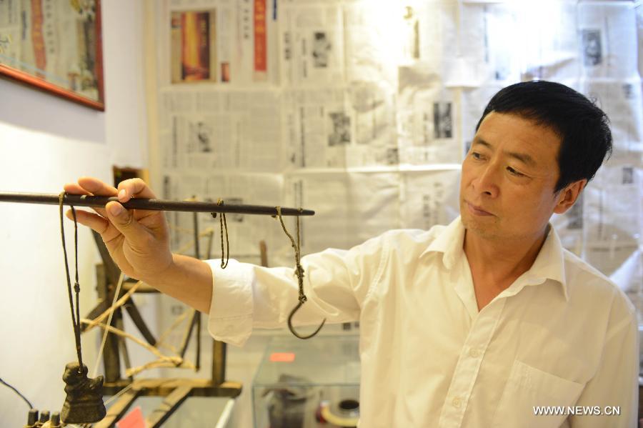 A man demonstrates a steelyard used in the old times in Yanzhangzi Village of the Man Autonomous County of Kuancheng, north China's Hebei Province, July 16, 2013. A museum collecting old stuff was set up in the village to remind the local residents of hard time in the old days. (Xinhua/Wang Min)