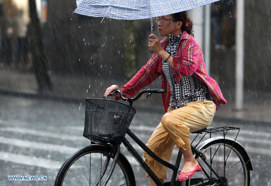 A resident rides in rain on Nanjing Road, east China's Shanghai, July 26, 2013. A rainstorm hit Shanghai Friday afternoon, bringing coolness to the scorching weather. (Xinhua/Yang Shichao)